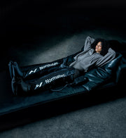 Person using Normatec compression boots on a dark background